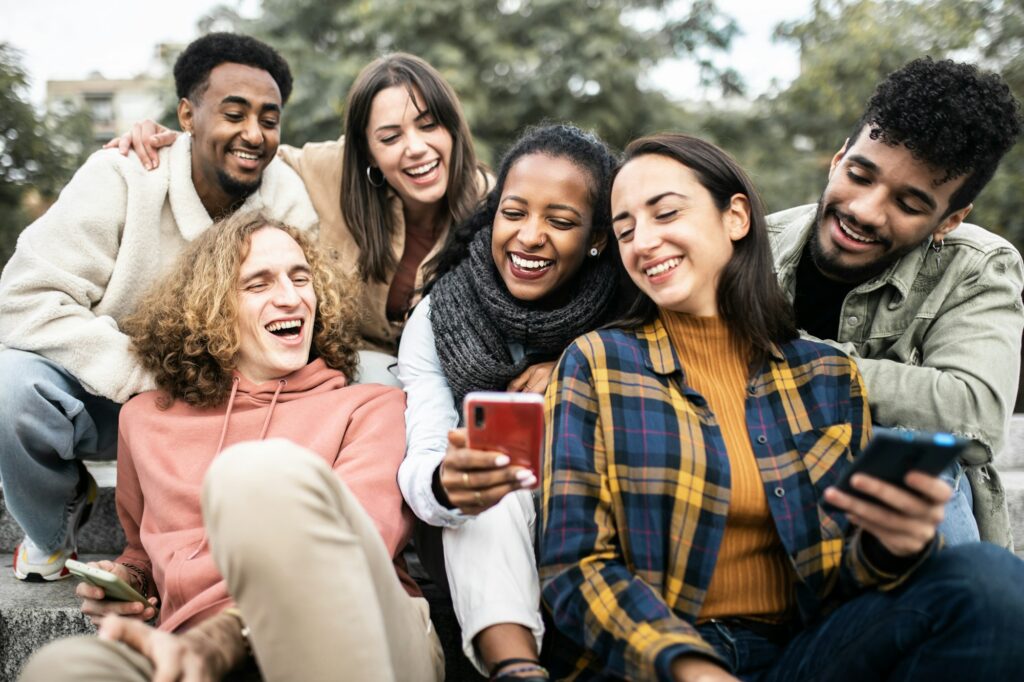Millennial multiracial friends using smartphone while sitting outdoors