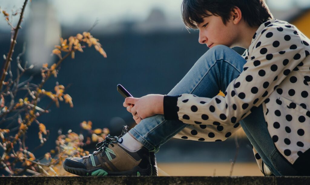 Side view of preteen girl with smartphone sitting outdoors in town